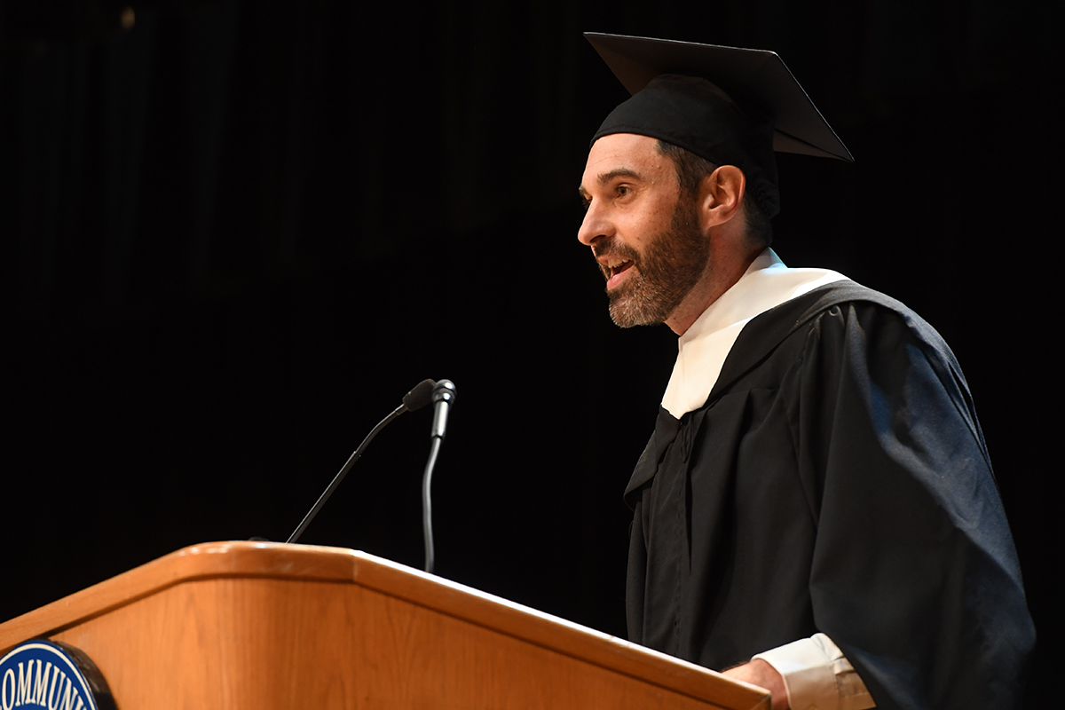 A professor stands over a podium giving a speech at a graduation ceremony.