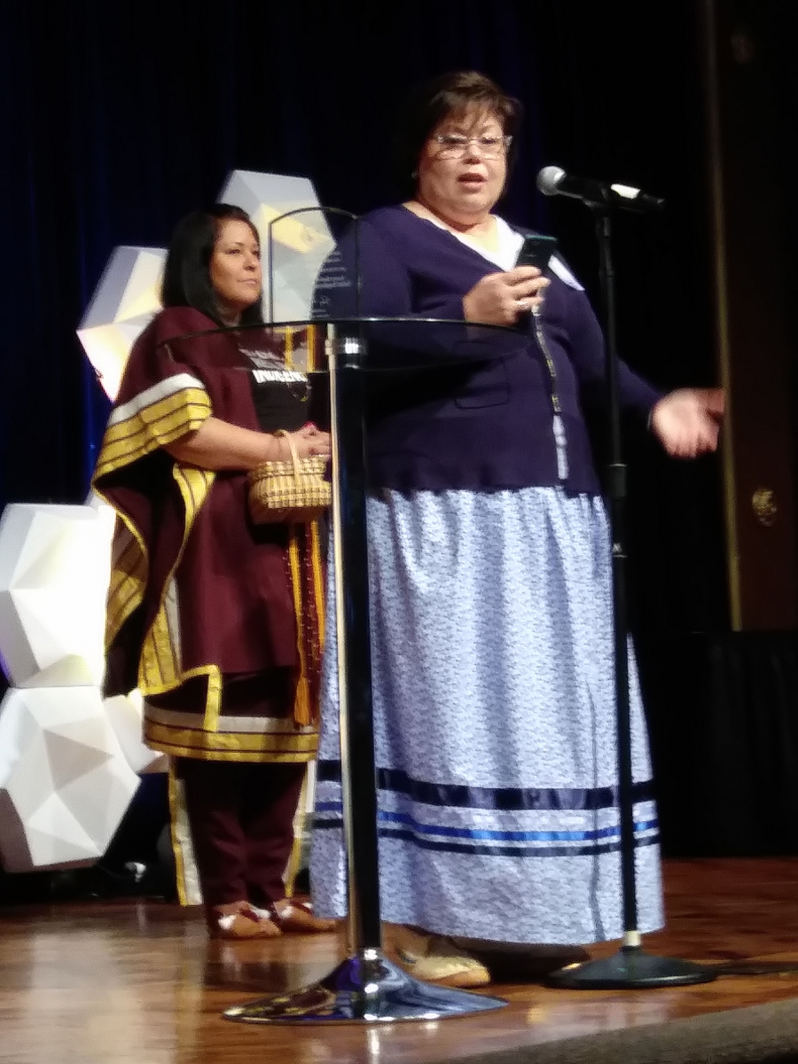 Woman standing to accept an award with another woman behind her.