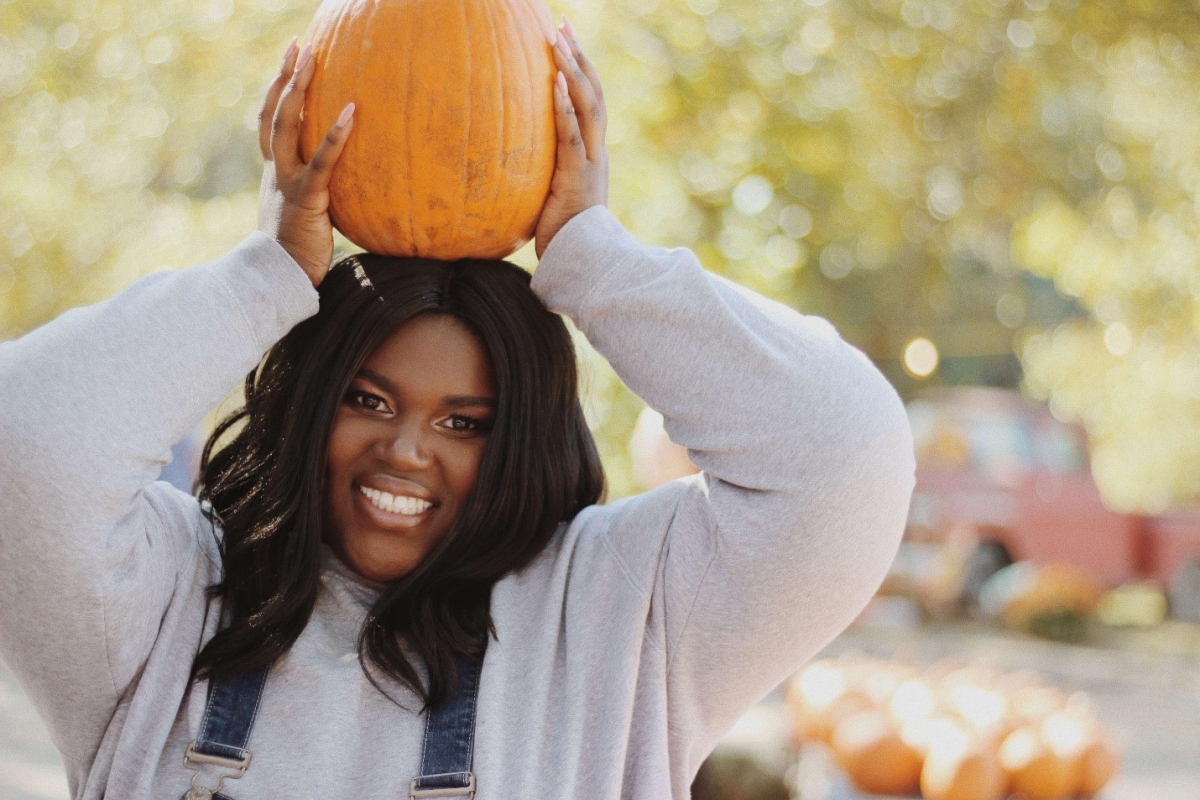 Student in gray sweatshirt holding pumpkin on top of her head.
