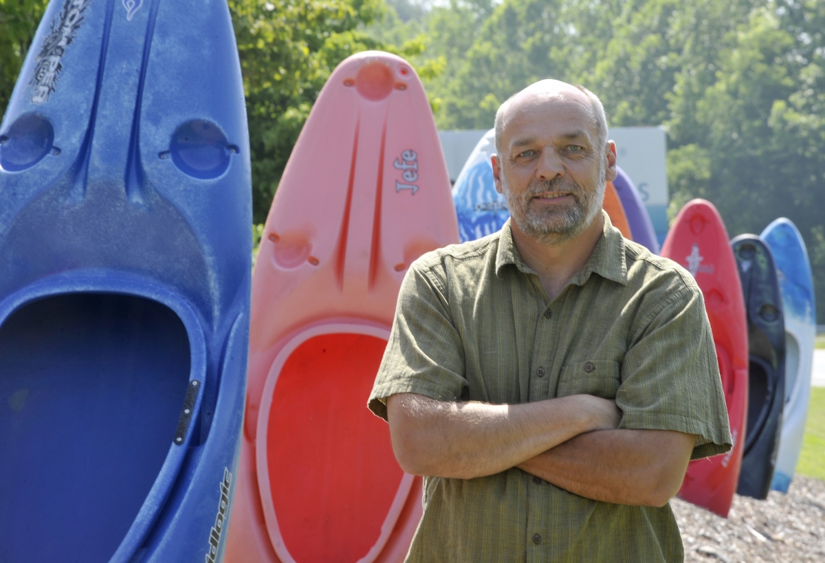 Man stands beside a row of kayaks outdoors