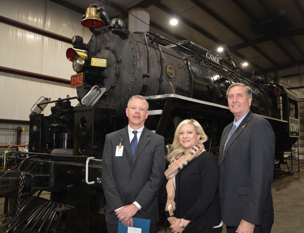 Two men and a lady stand in front of a recently renovated steam locomotive.