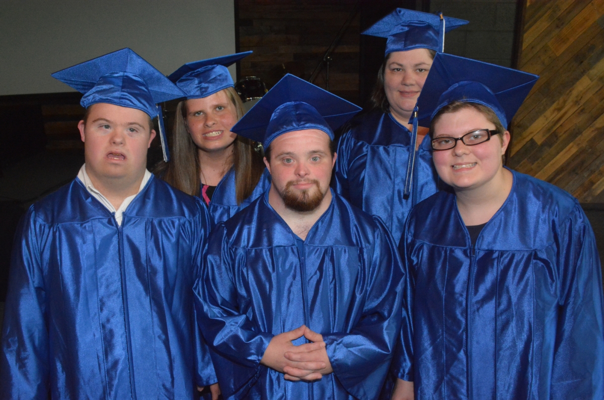 Five graduates wearing blue robes and caps smile for the camera.