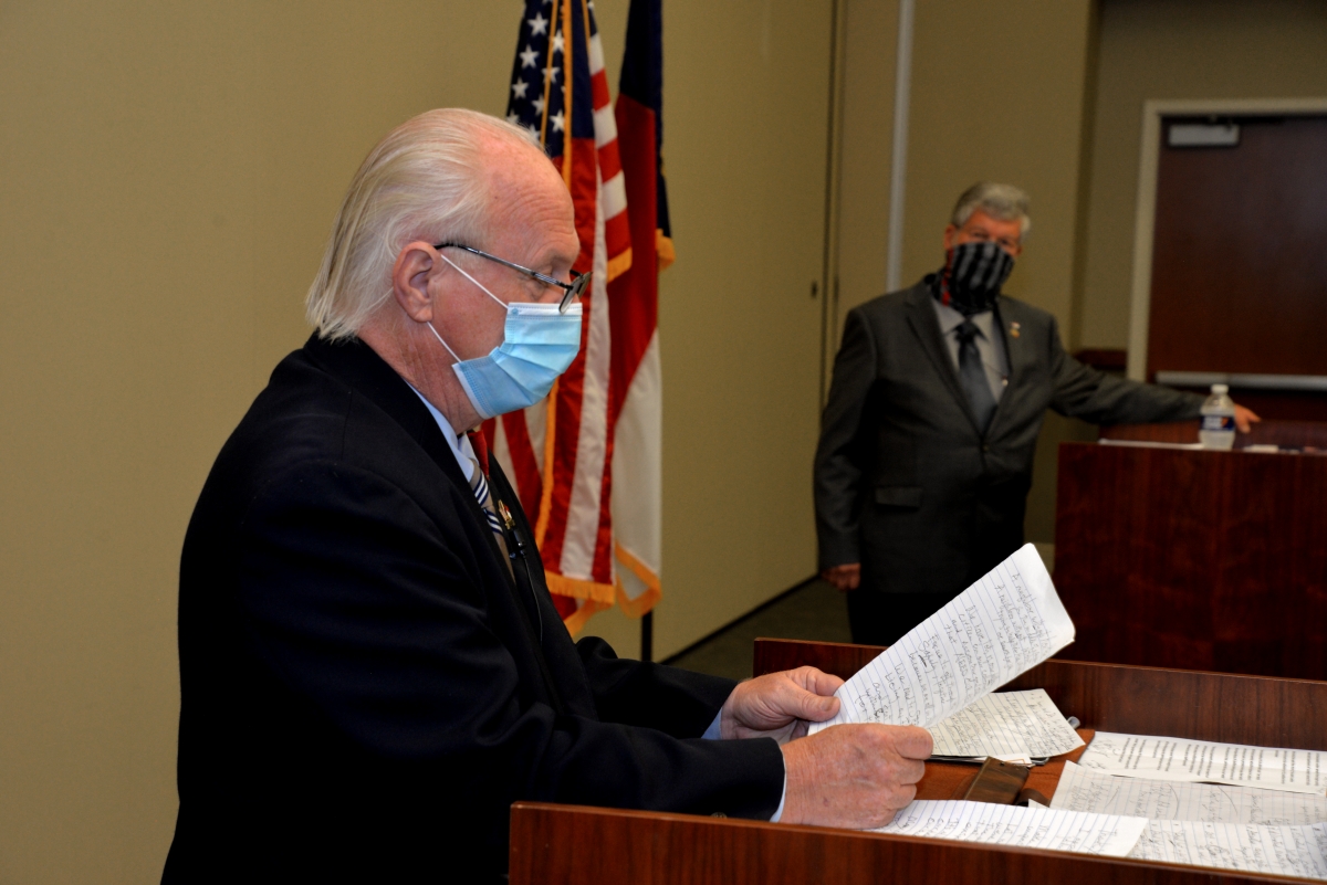 Two men wearing masks stand at podiums