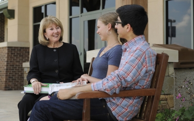 Woman sits on outdoor bench, chatting with students