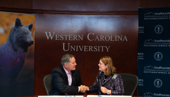 Dr. Brown & Dr. Tomas shake hands at a board room table..