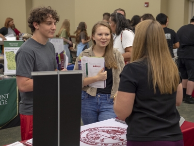 Young man and woman standing in front of a college fair booth.