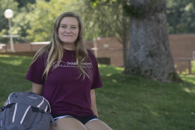 Young, blonde female student sits outside with her backpack on a sunny summer day.
