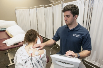 Young man placing electrical stimulation pads on the back of a young woman as part of physical therapy treatment.