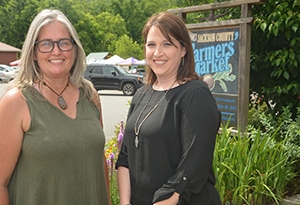 Two women stand together smiling at a local farmers market.