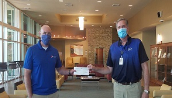 Two gentleman shake hands while wearing masks and standing apart