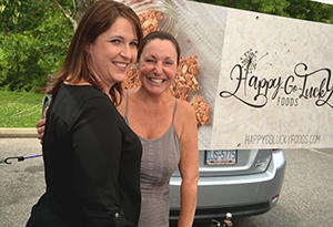 Two women stand together smiling at a local farmers market.