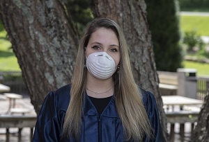 A young woman in a graduation gown is wearing a mask