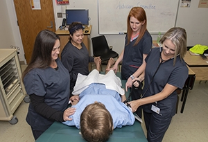 Group of female students in scrubs provide medical assistance to a patient on a table.