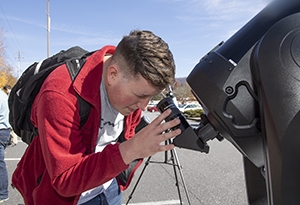 Young man looks into telescope to view Mercury cross in front of the sun.