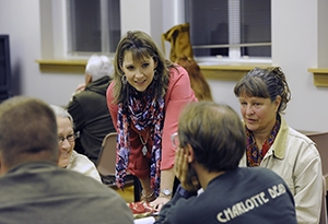 Business woman leans over a table while speaking to a group of seminar attendees.