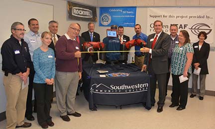 Photo of Dr. Don Tomas, president of Southwestern Community College helps Randy Lomax, Bryson City plant manager for ConMet stretch out a ribbon for Baxter the Robot to cut at the grand opening of Southwestern Community College’s Advanced Manufacturing Education Lab