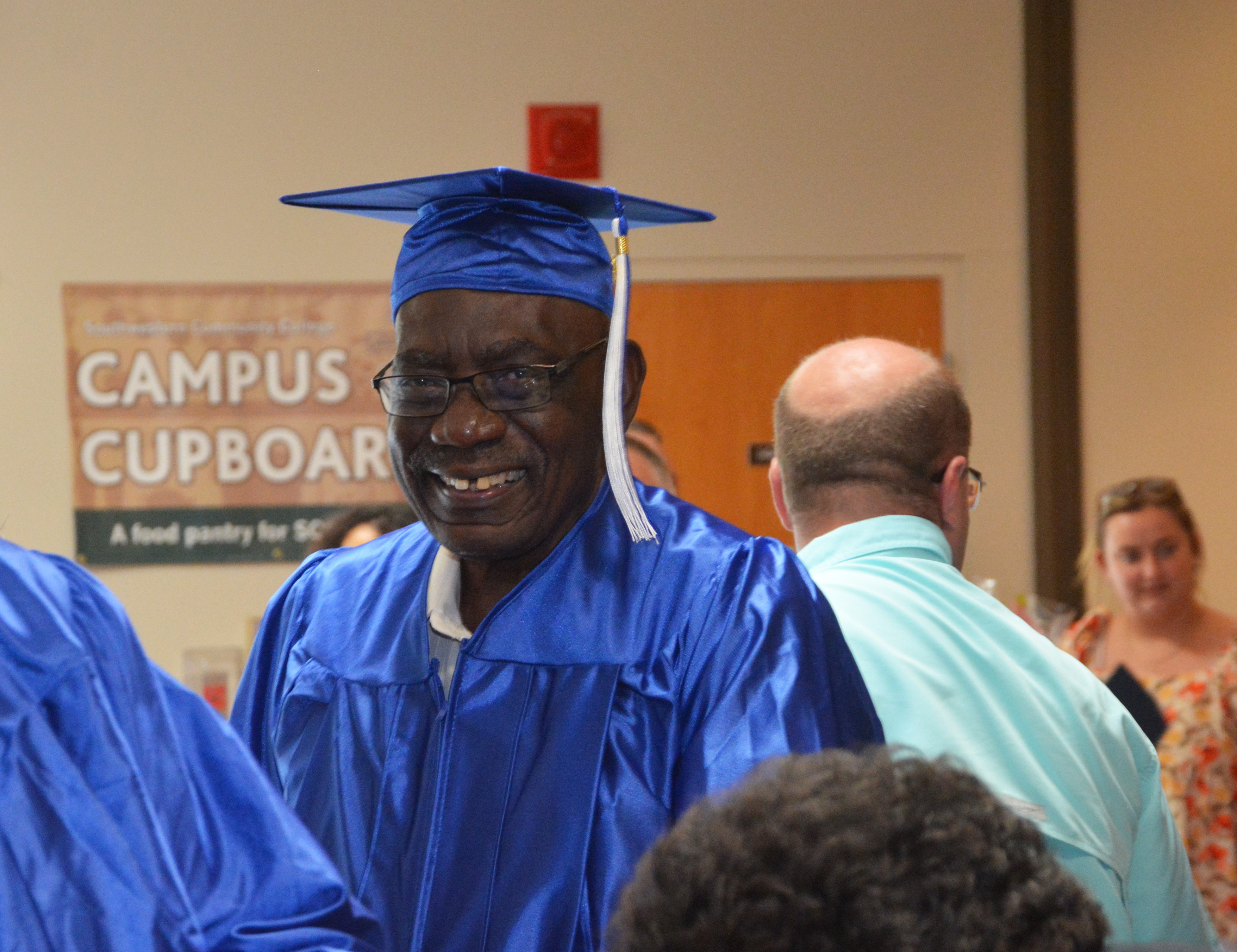Calbert Christian smiles wearing blue graduation cap and gown