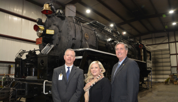 Two men and a woman stand in front of a recently renovated steam locomotive.