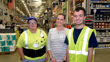 Two men and a woman stand indoors at Lowe's store with aisles and customer service desks in background