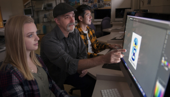 Instructor works with two students at computer monitor