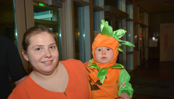 A young lady holds a child wearing a pumpkin costume.