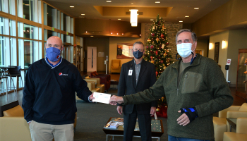 Two men exchange a check while a third stands behind them. All three are social distancing and wearing masks.