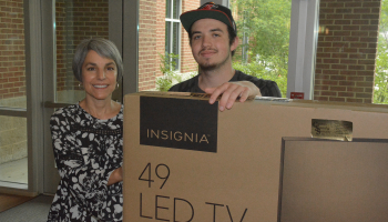 Man and woman hold a cardboard box that contains a flat-screen TV.