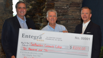 Three men pose with a large check next to stacked rock.