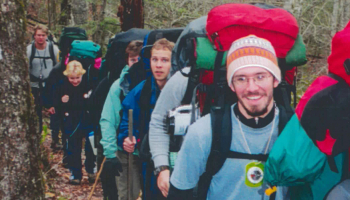 Students wearing backpacks hike outdoors.