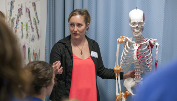 Woman stands next to skeleton, teaching students about therapeutic massage