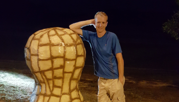 Man stands beside large peanut statue