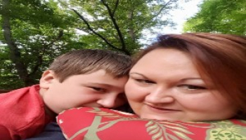 A woman and her son take a selfie underneath some trees outside