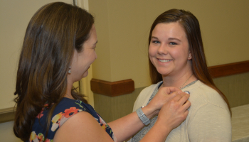 A student smiles at the camera as her instructor pins her