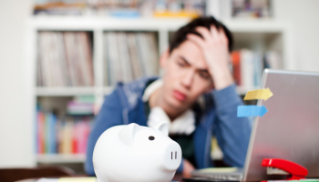 Student holds his hand to his head and looks depressed as he stares at a piggy bank