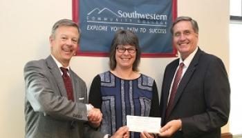 A woman smiles while shaking hands with two men and presenting a check