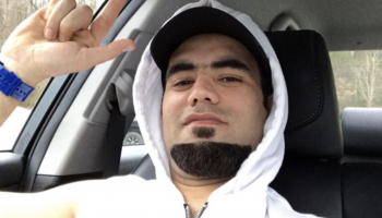 Young man in hoodie sits in his car throwing up playful hand gesture.