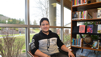 Young man smiles while sitting in front of a window at a library