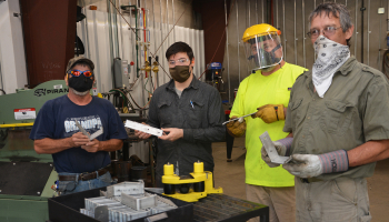 Men hold pieces of metal while wearing protective face gear