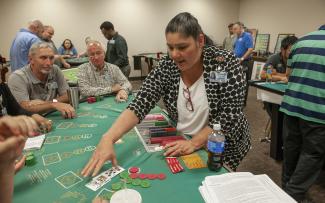 Woman deals a hand of blackjack to several classmates inside a casino training room.