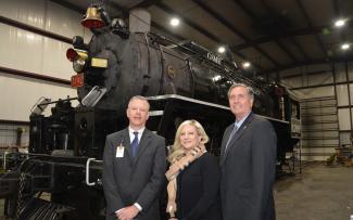 Two men and a woman stand in front of a recently renovated steam locomotive.
