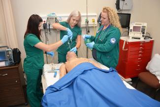 Three female students wearing turquoise scrubs practice their respiratory therapy skills on a simulation mannequin inside a room on SCC's Jackson Campus in Sylva.