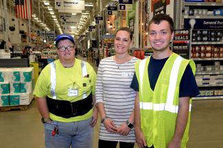 Two men and a woman stand indoors at Lowe's store with aisles and customer service desks in background