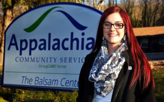 Lady stands outdoors in front of a "Balsam Center" sign