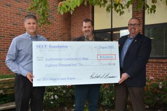 Three men hold up an oversized check
