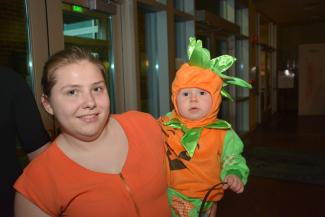 A young lady holds a child wearing a pumpkin costume.