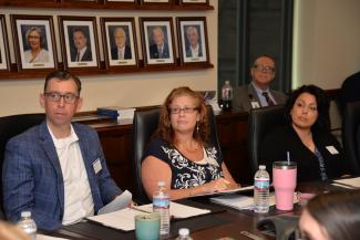 Three employees sitting at board room table listen to a presentation.