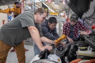 Three students look under the hood of a car