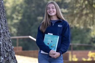Student holds book and poses on campus