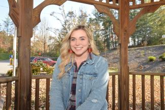 Young woman smiles underneath a gazebo on a sunny fall day.