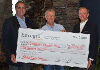 Three men pose with a large check next to stacked rock.